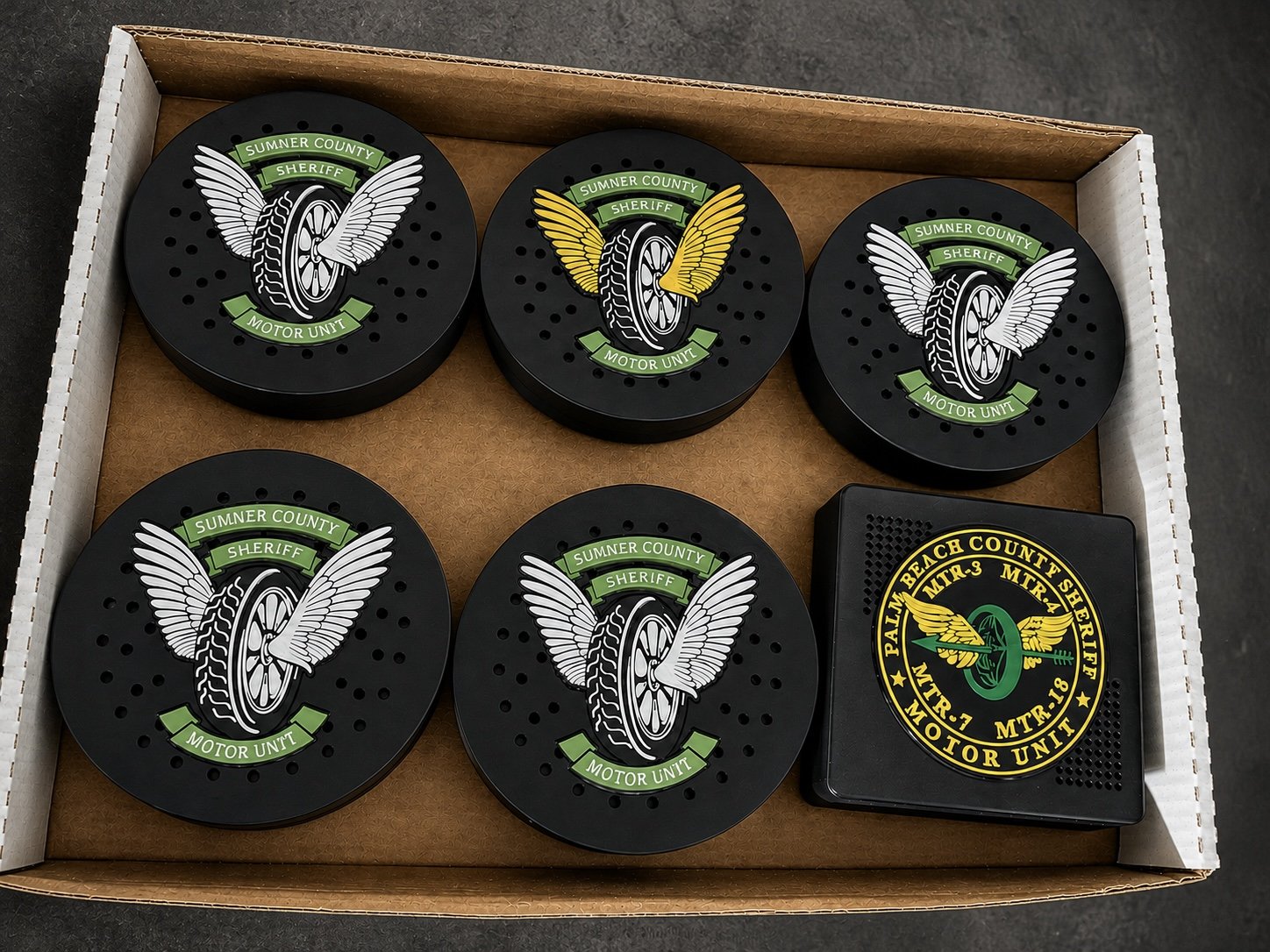 Box of black police siren covers with green and white winged emblems