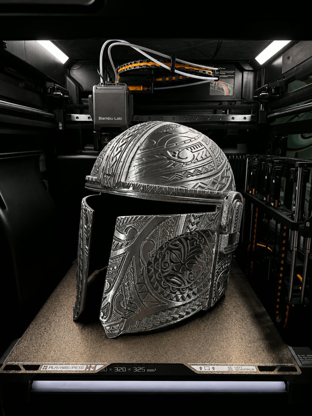 Silver Mandalorian-style helmet with engraved patterns on the printer bed