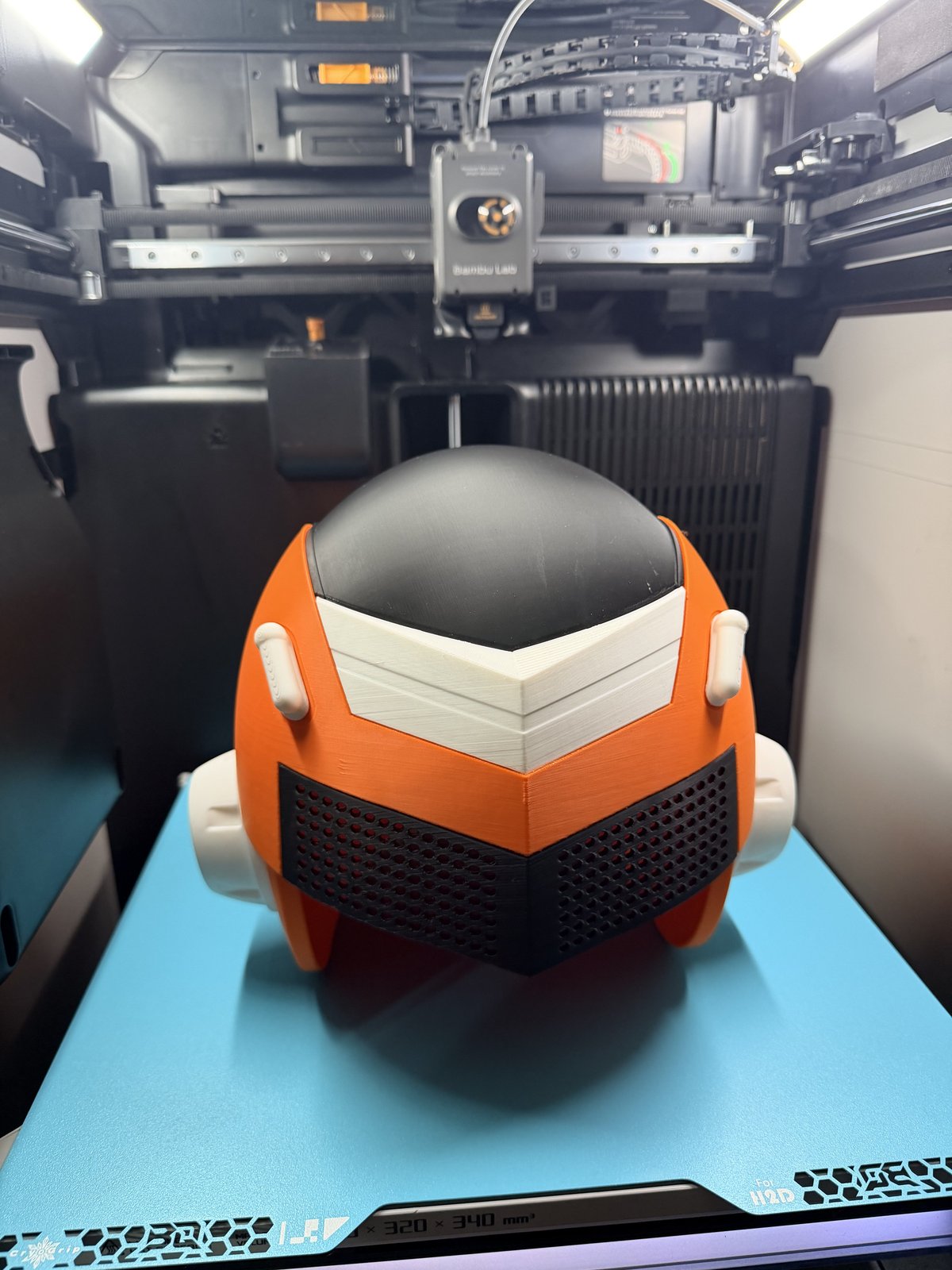 Orange, black and white sci-fi helmet printed on the printer bed